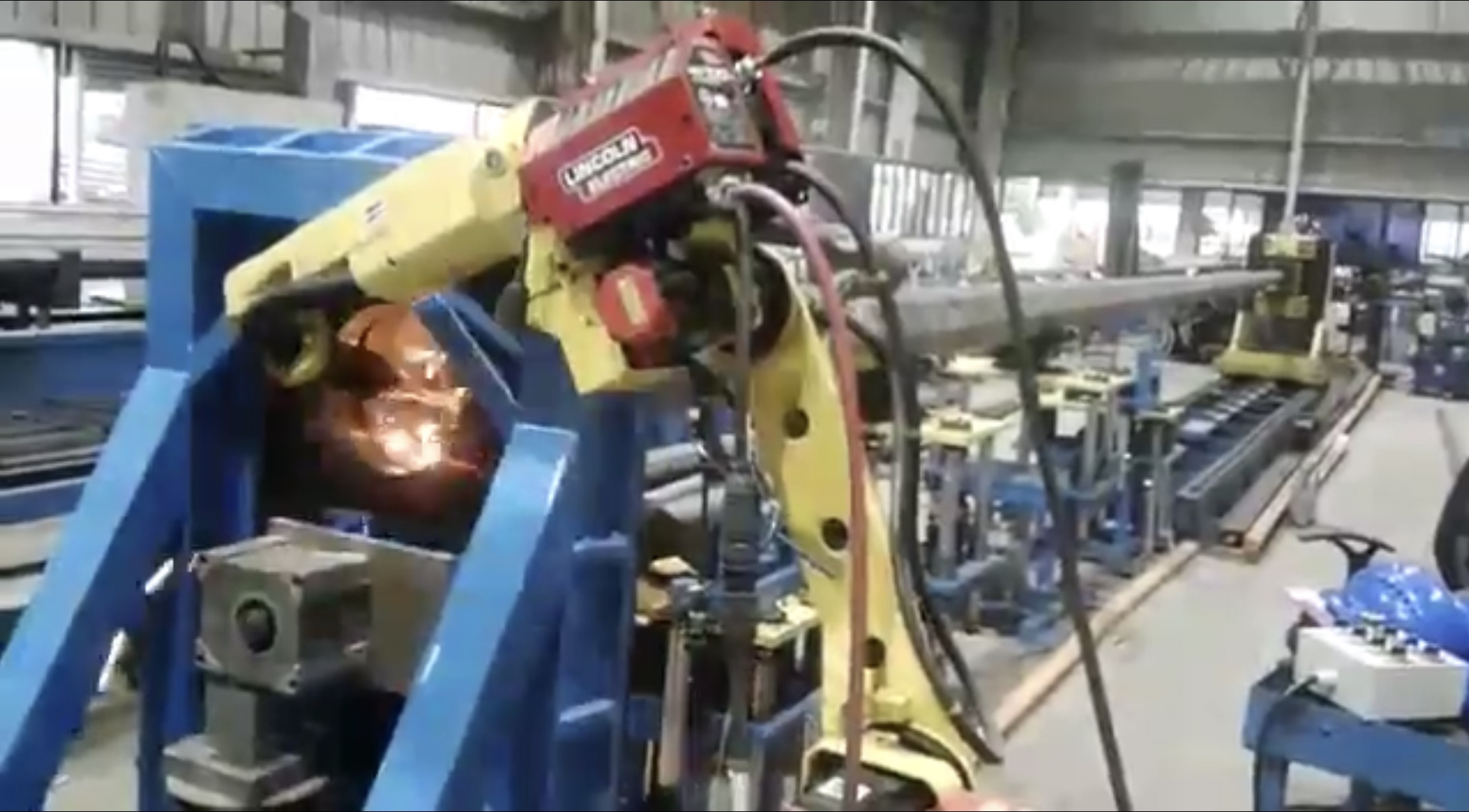 A robotic welding cell mid-arc on a manufacturing floor